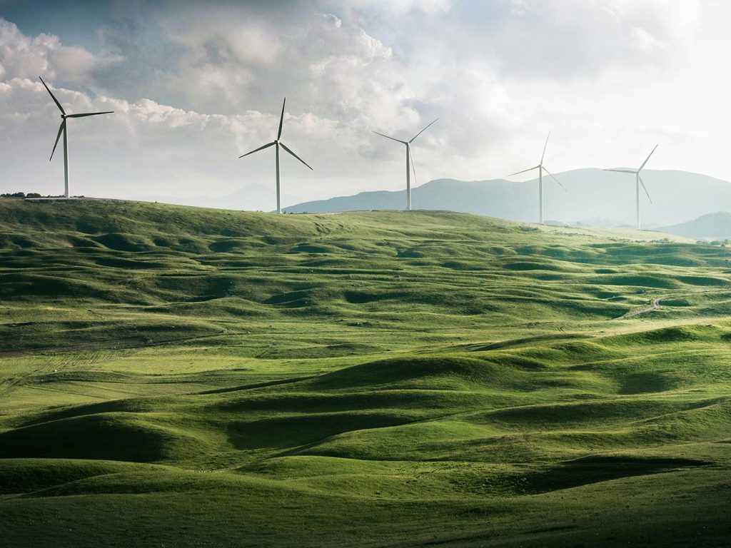 Windmills in&nbsp;a rolling green field overlooked by a mountain